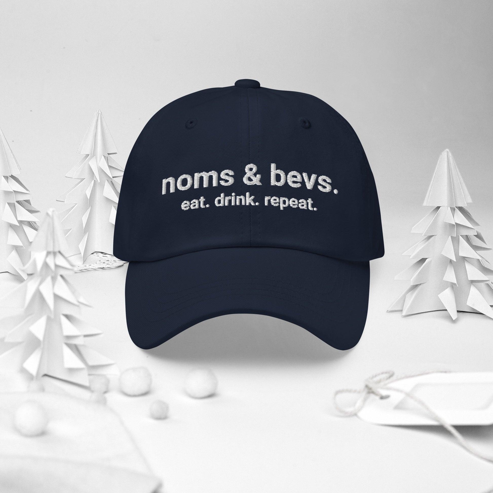 Navy blue hat with Noms & Bevs embroidered on the front. Underneath is "eat. drink. repeat." embroidered.