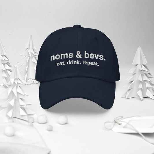 Navy blue hat with Noms & Bevs embroidered on the front. Underneath is "eat. drink. repeat." embroidered.